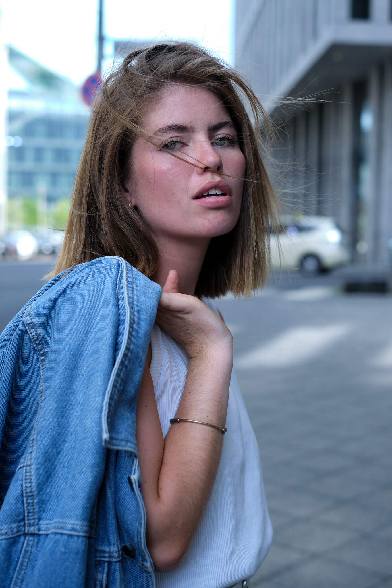 portrait of a young woman walking through the city streets holding a denim jacket over her shoulder